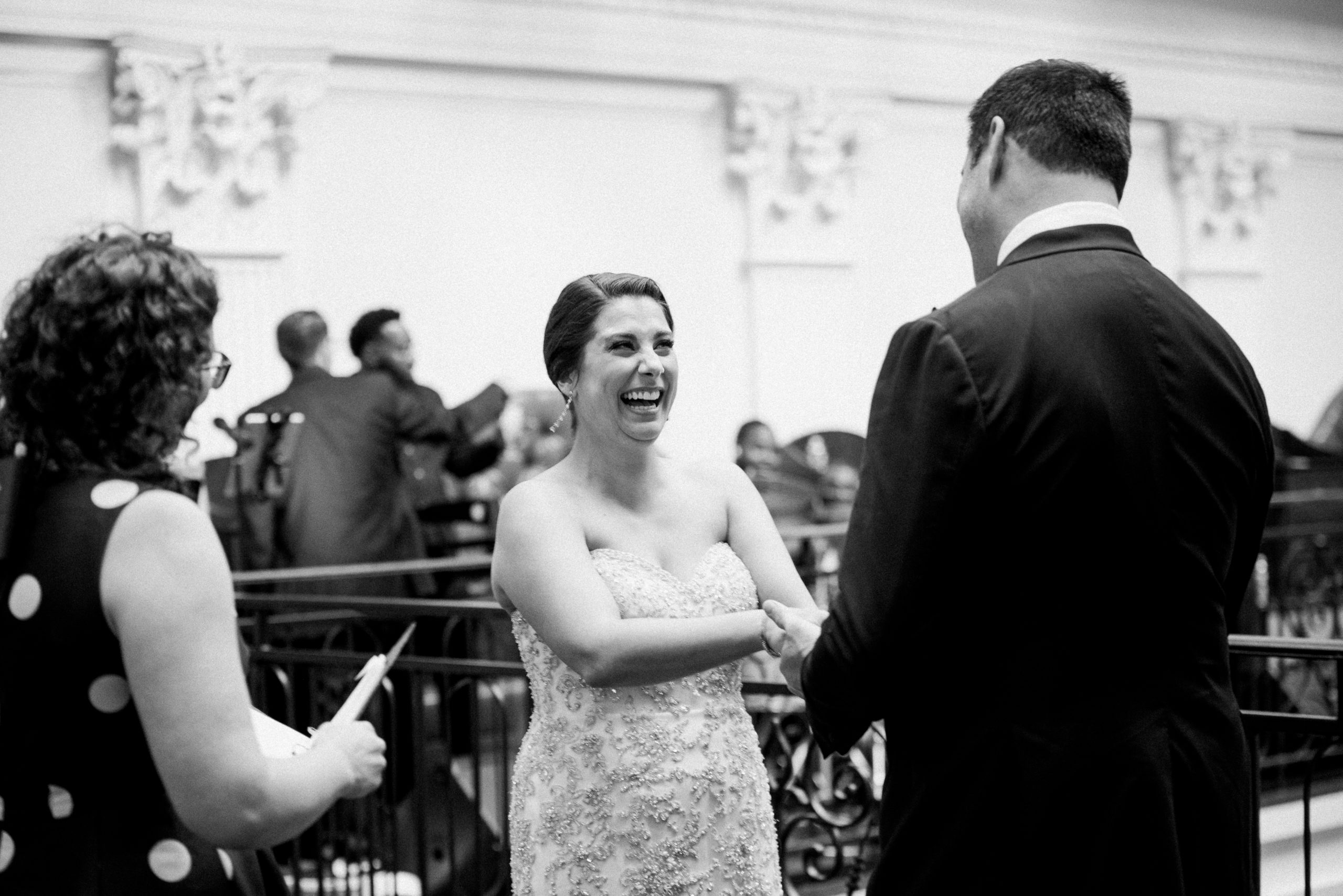 A black and white picture of the bride with laughing and holding the hands of the groom