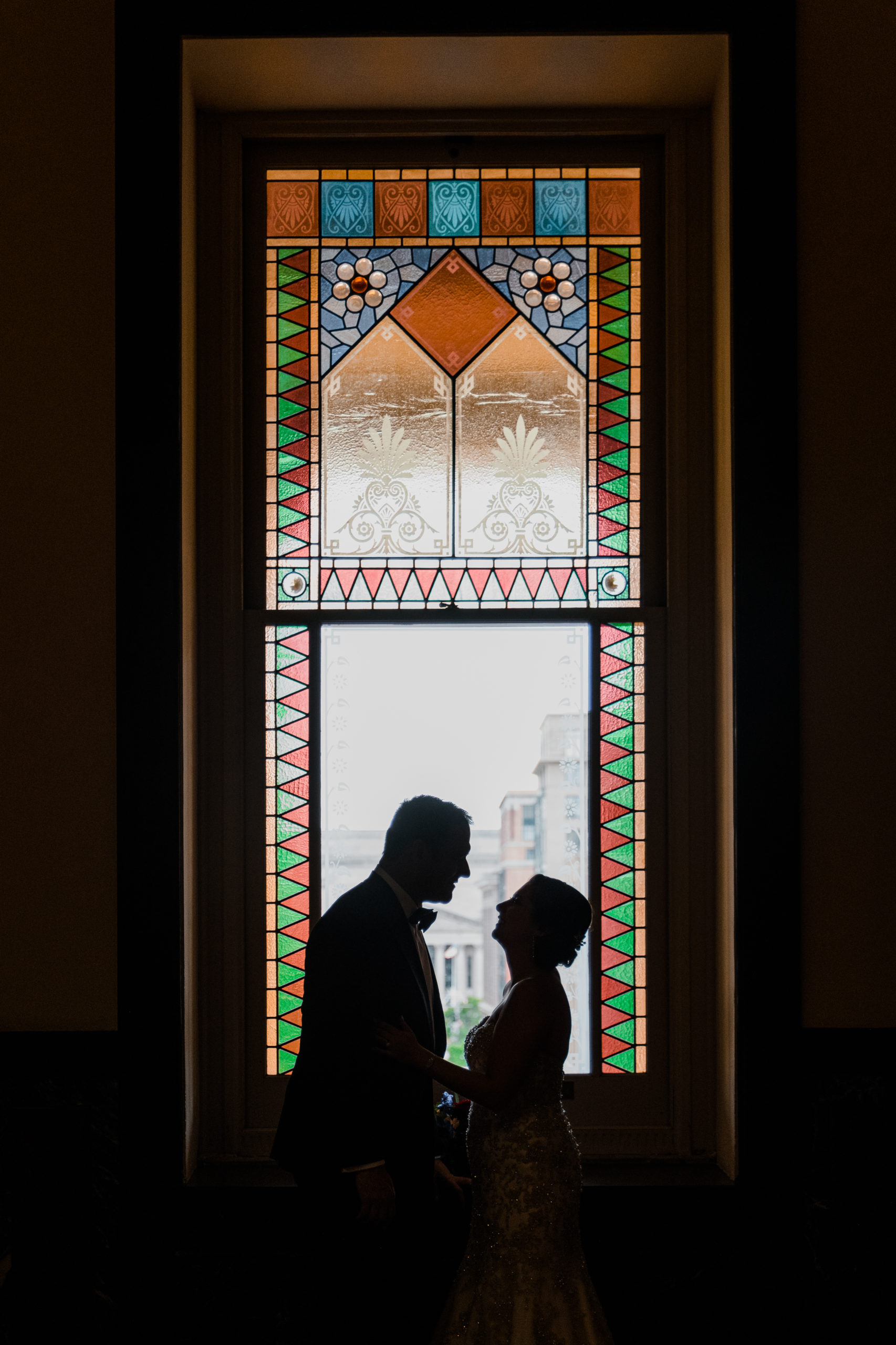 The bride and groom posing in front of a stained glass window