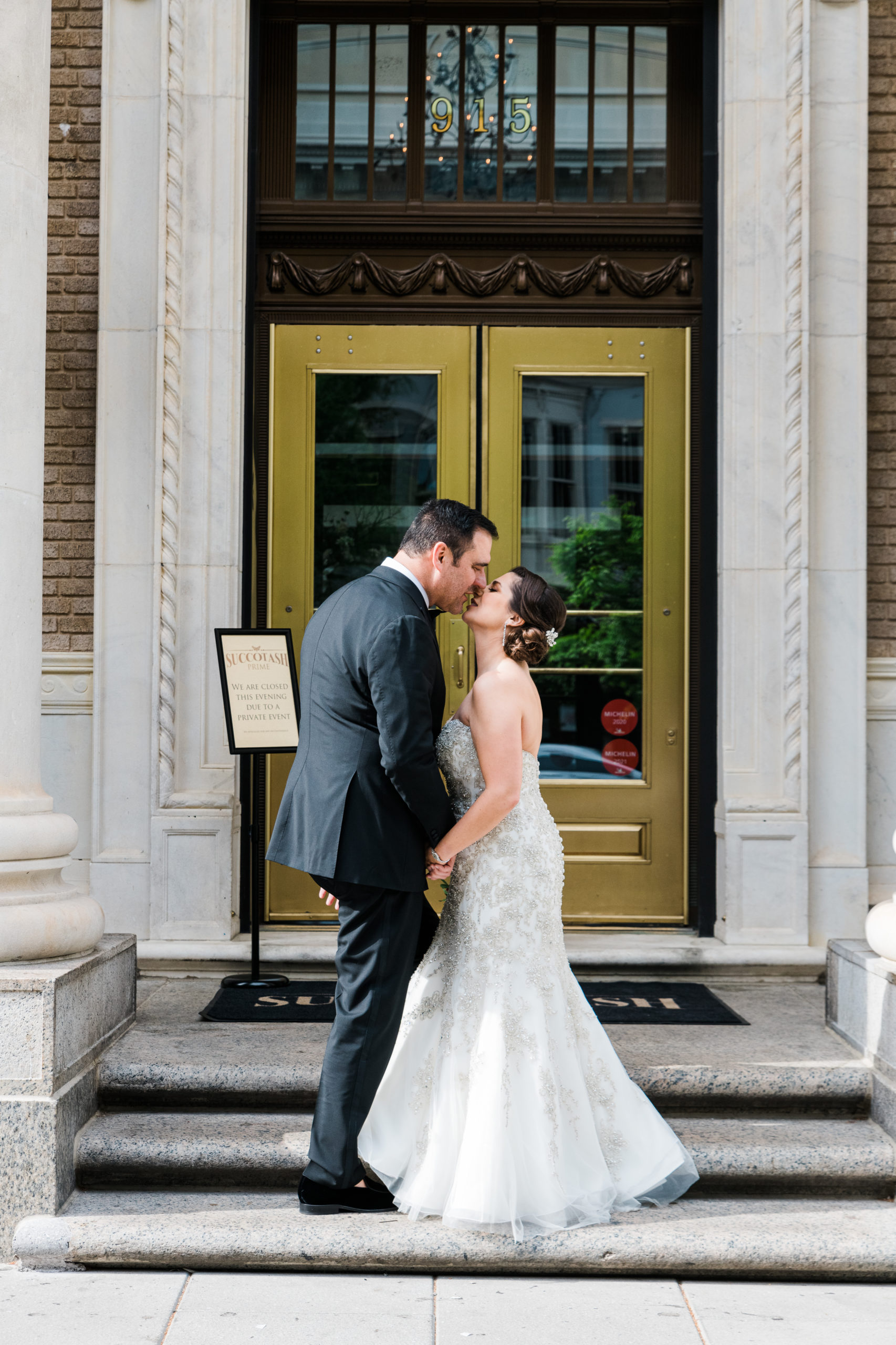 The bride and groom kissing on the steps in front of Succotash Prime restaurant in Washington DC
