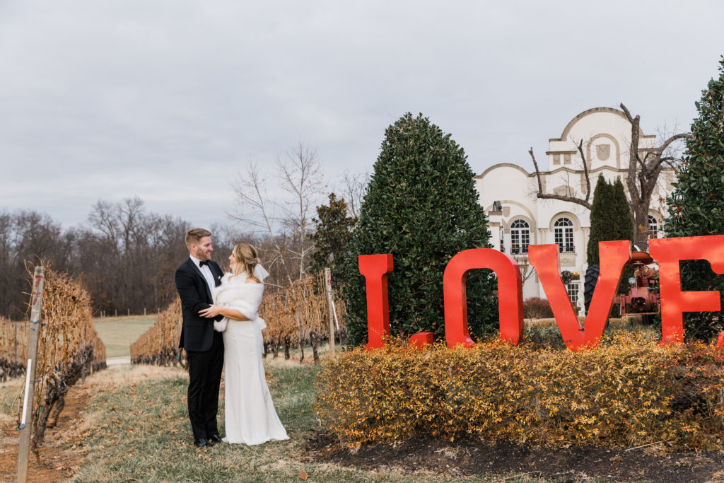A bride and groom hugging in front of a large red "Love" sign at Morais Vineyards and Winery