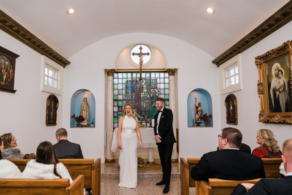 A bride and groom standing at the front of a church in front of wedding guests