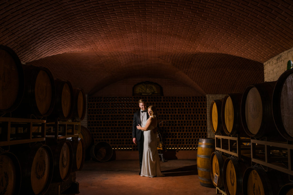 A bride and groom posing in the cellar of Morais Vineyards and Winery