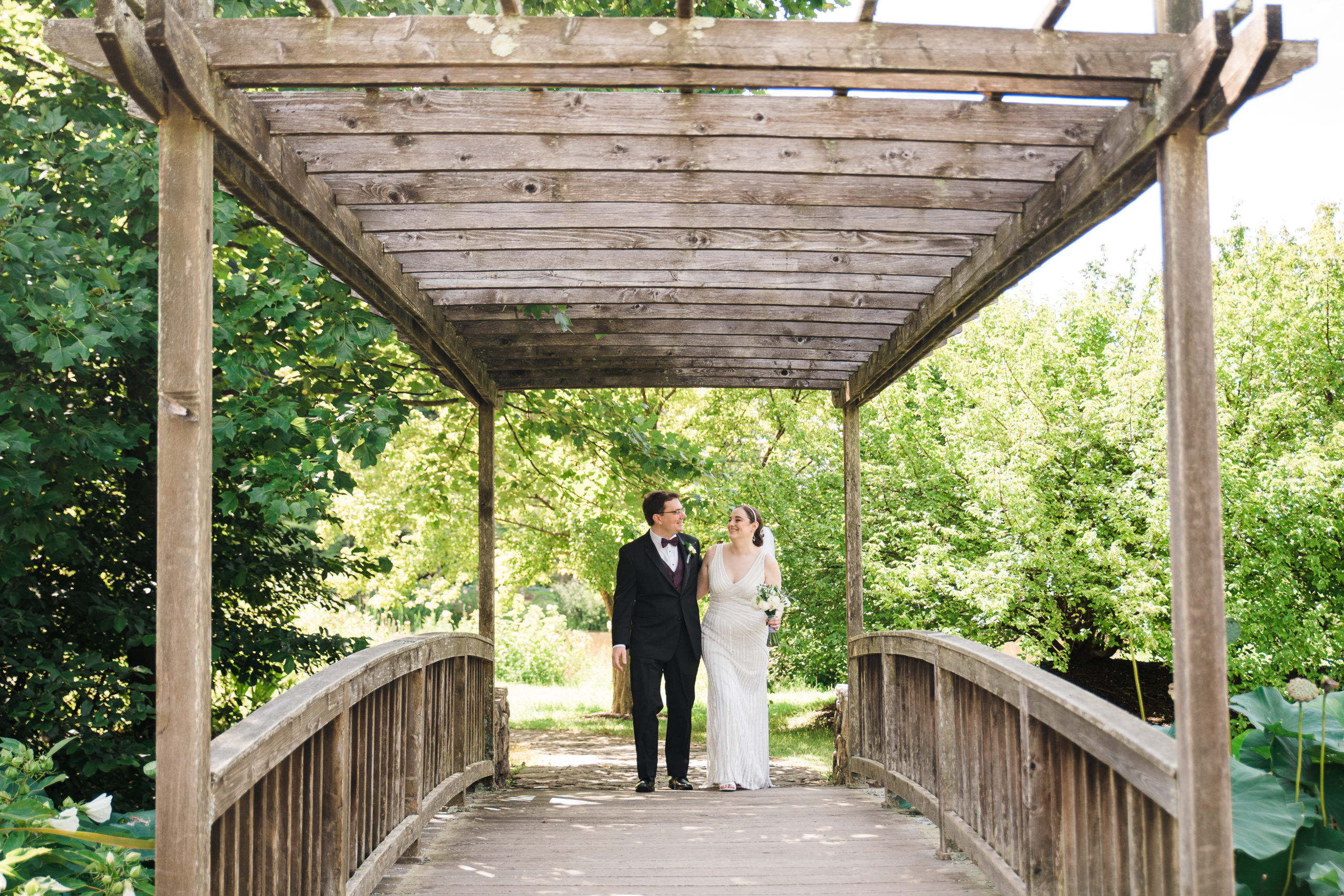 Bride and groom walking hand in hand on a bridge at the Atrium at Meadowlark Botanical Gardens