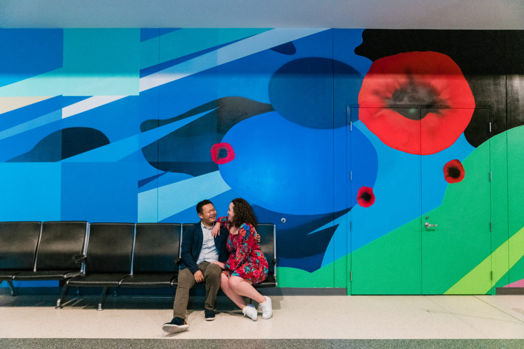 A couple sitting on a bench in front of a large wall mural at the Smithsonian Arts and Industries Building