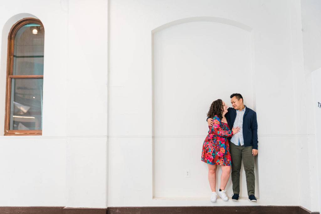 Couple standing in front of a white wall posing for engagement pictures at the Smithsonian Arts and Industries Building
