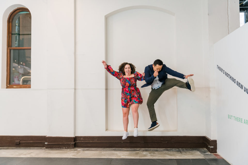 A man and a woman jumping in front of a white wall at the Smithsonian Arts and Industries building