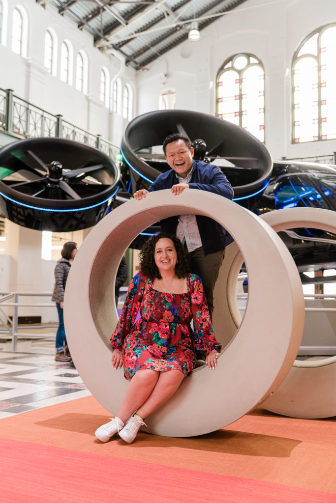 A woman sitting in a round sculpture with a man posing behind her at the Smithsonian Arts and Industries Building