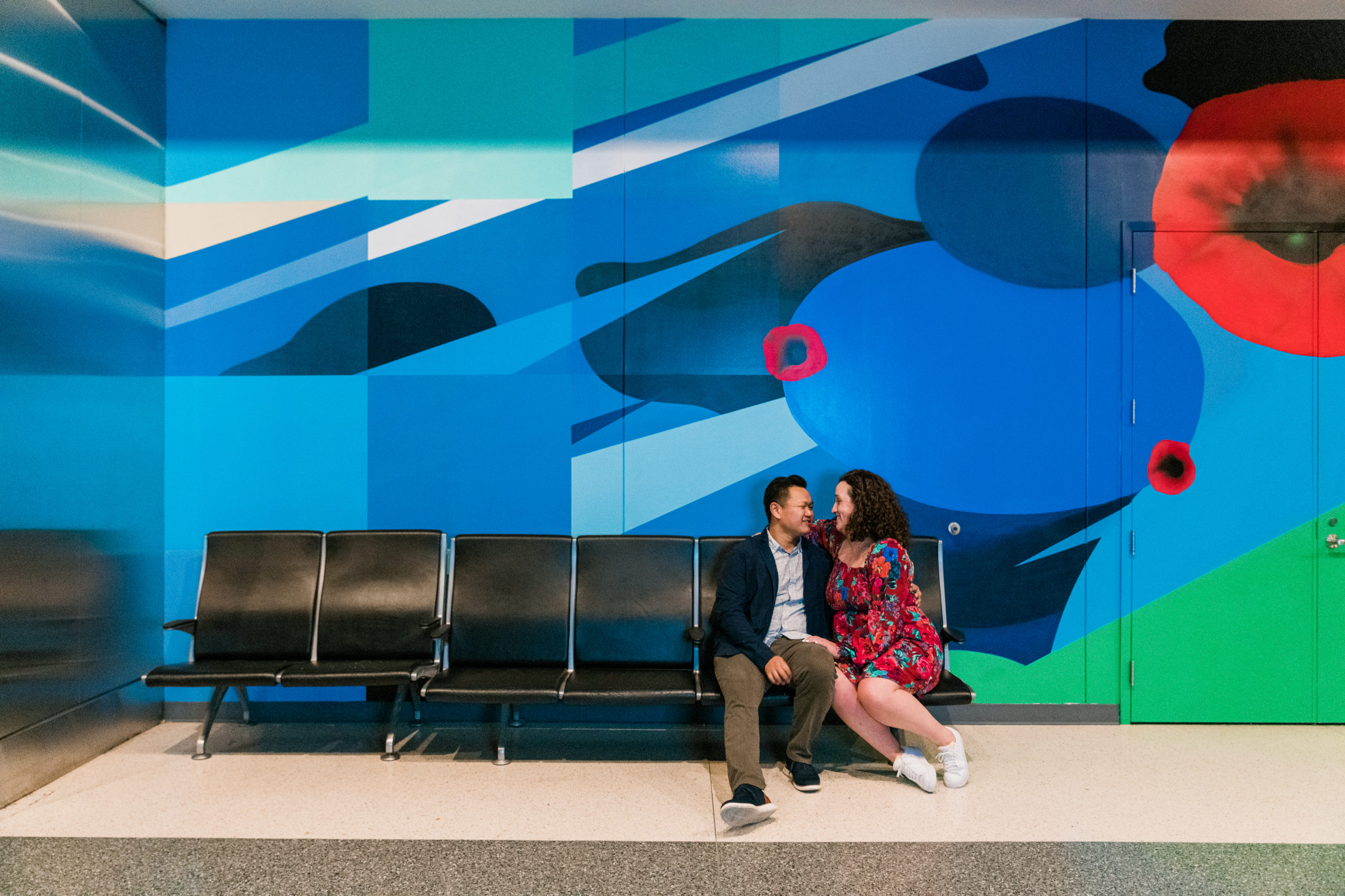 A man and a woman sitting on a bench in front of a wall mural at the Smithsonian Arts and Industries Building