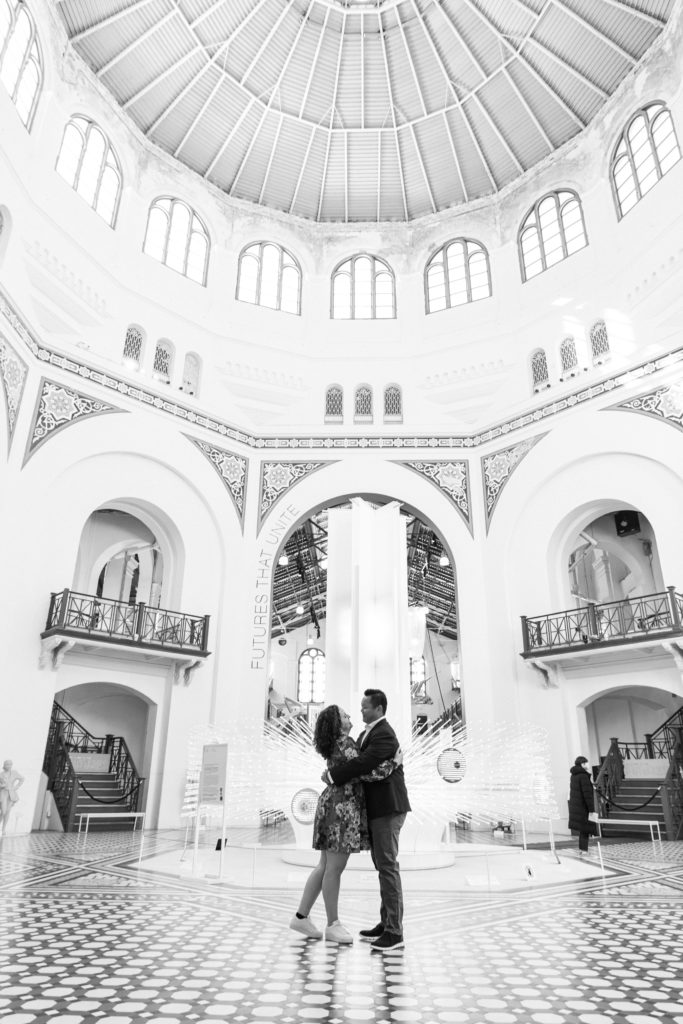 Couple hugging and standing in the middle of a large atrium at the Smithsonian Arts and Industries Building