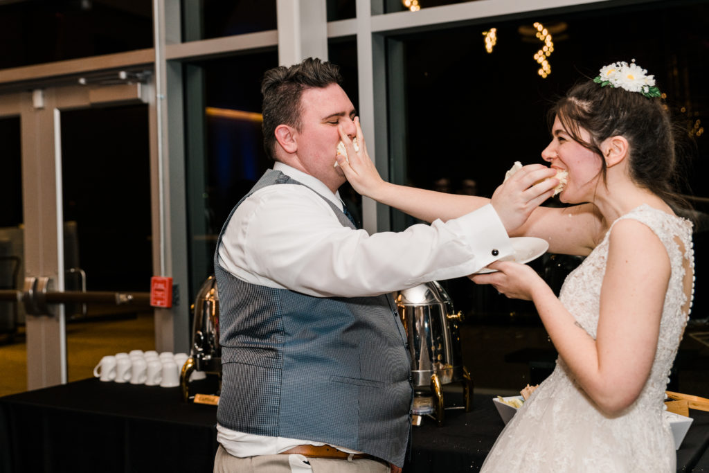 Bride and groom smooshing cake in each others faces during a wedding reception at the River View at Occoquan