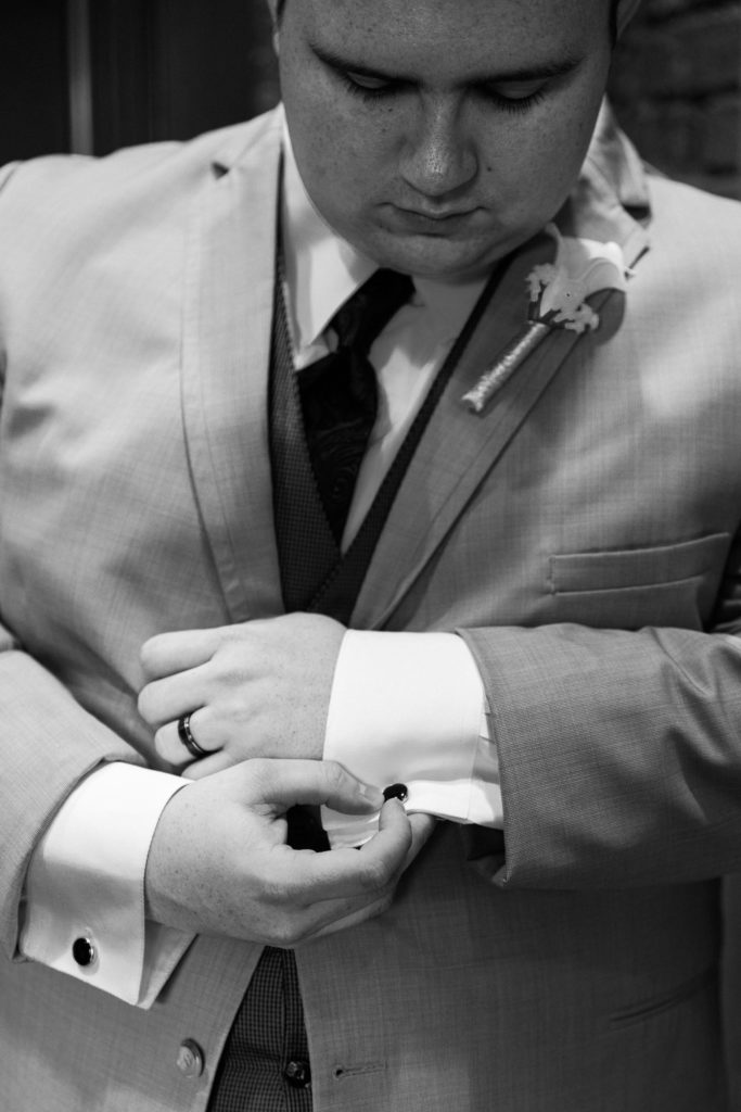 Close up of a groom buttoning his cuff links