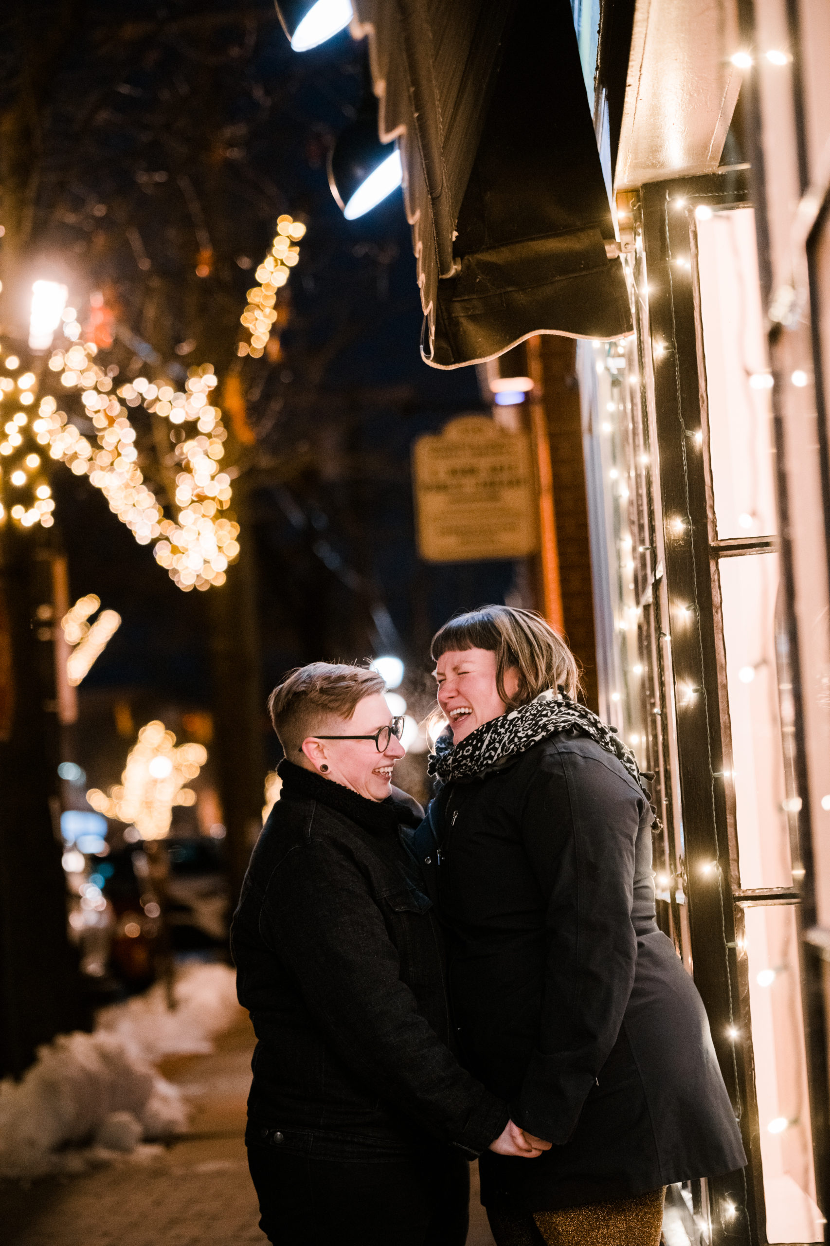 A couple embracing outside with holiday lights in the background