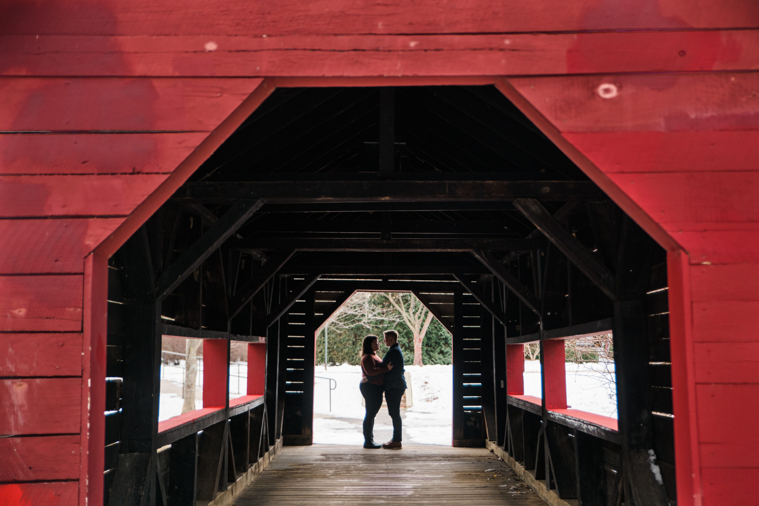 A couple standing and facing each other in a red covered bridge