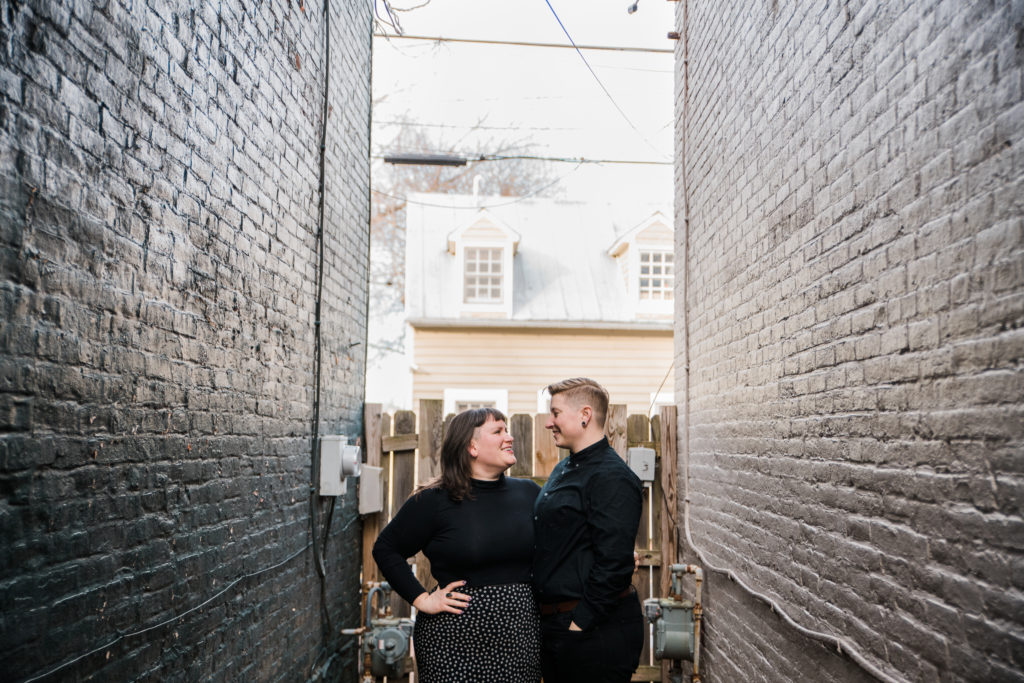 A couple gazing at each other while standing between two brick walls in Frederick, MD