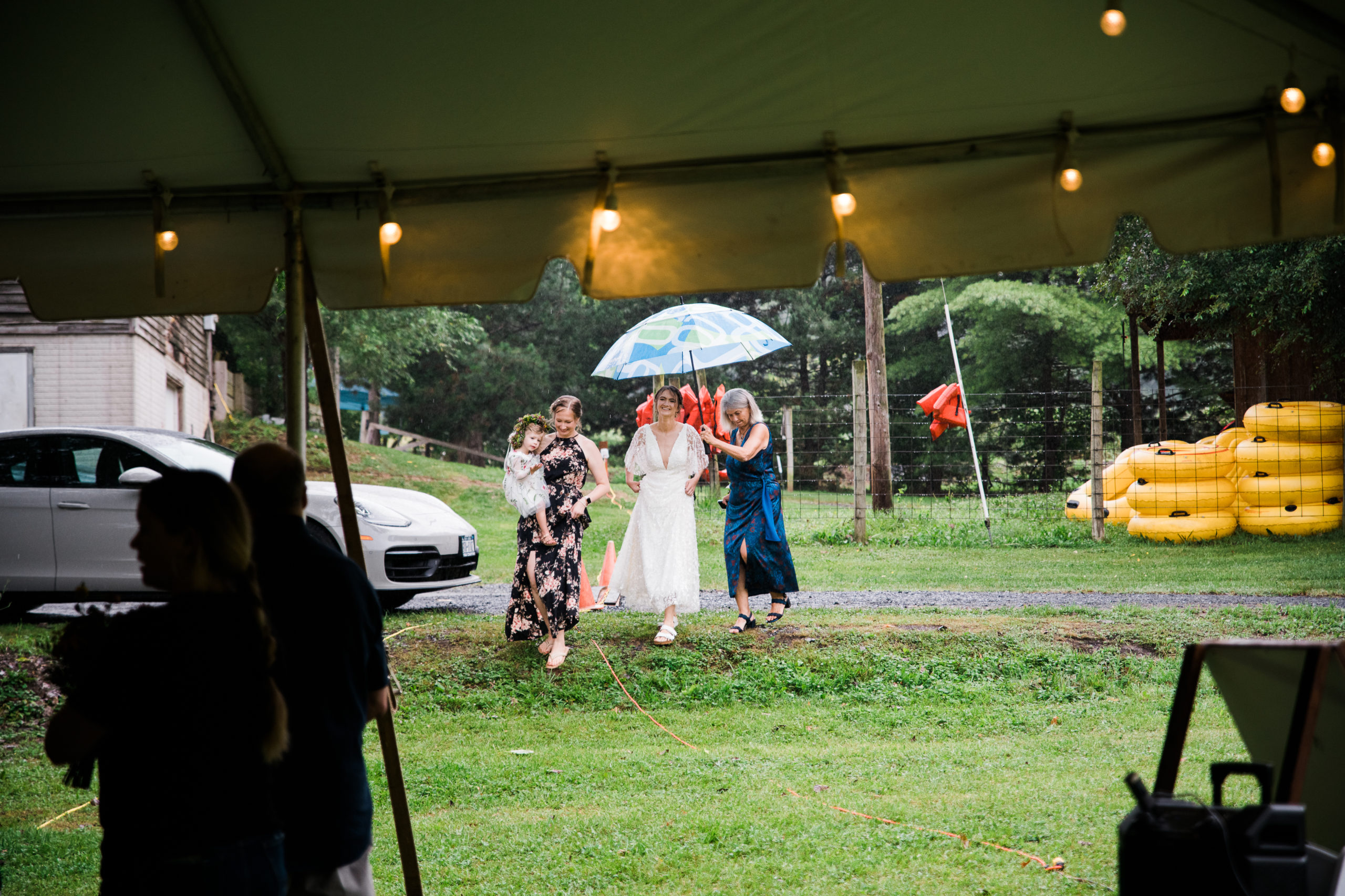 The bride arriving at a wedding ceremony with two women holding an umbrella over her head
