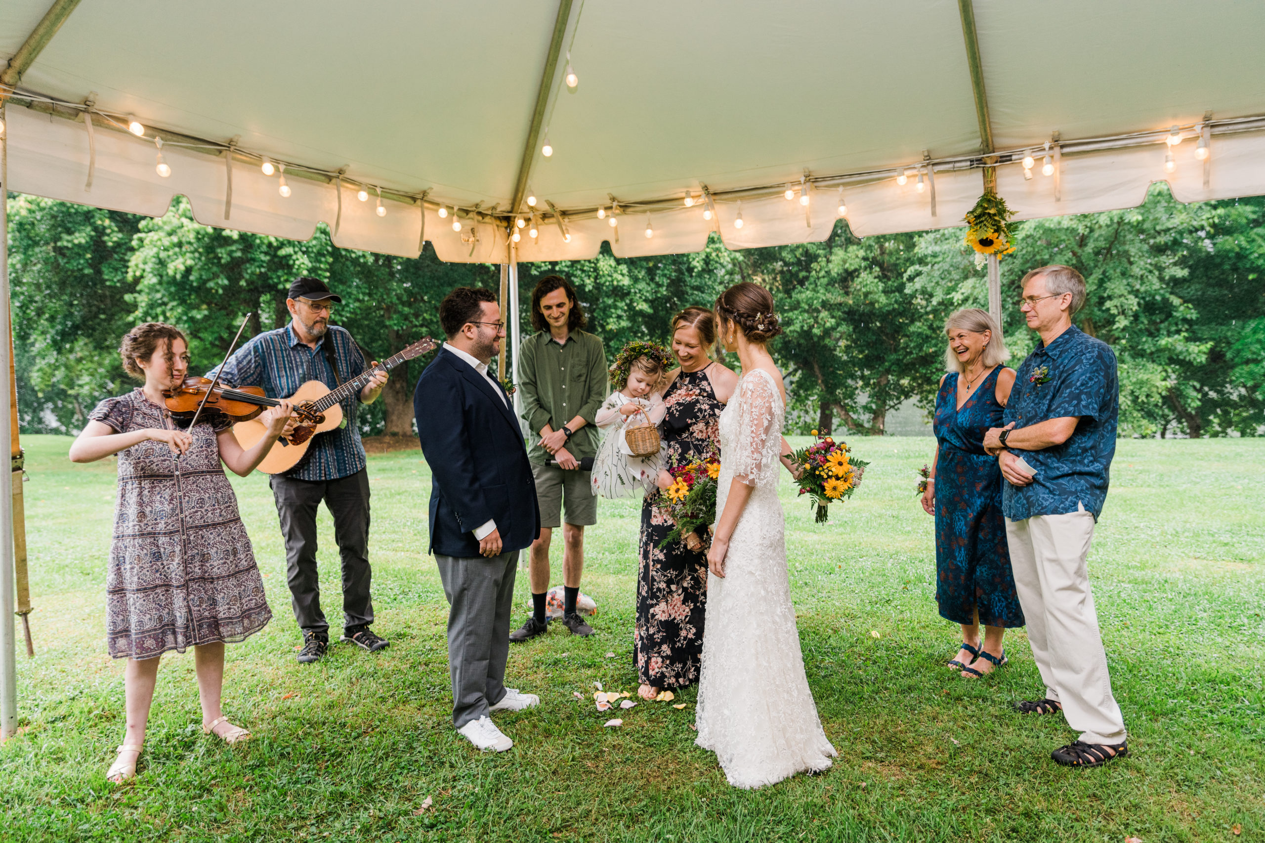 A bride and groom standing under a tent surrounded by musicians playing instruments
