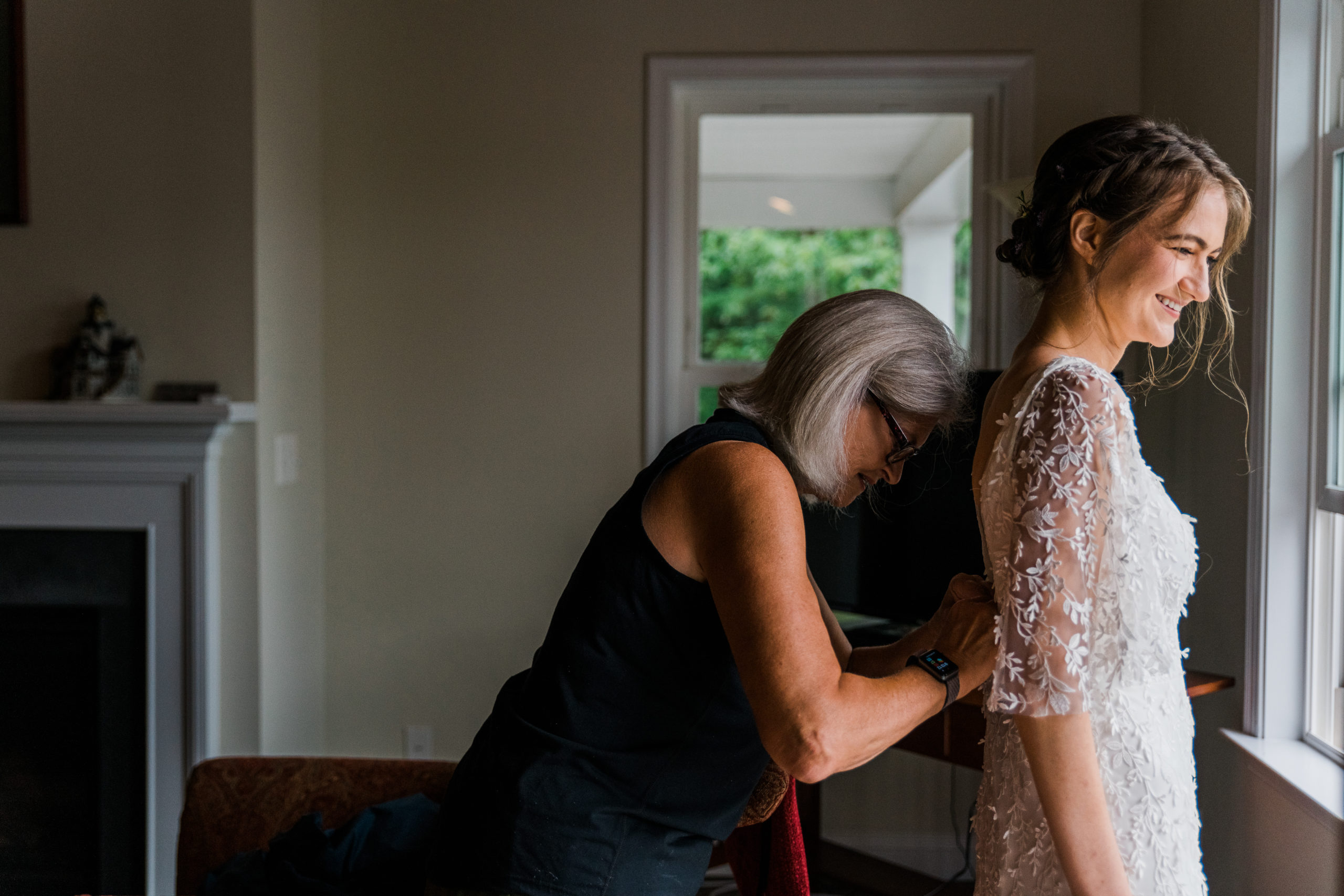 A woman helps zip up the back of a bride's white wedding dress