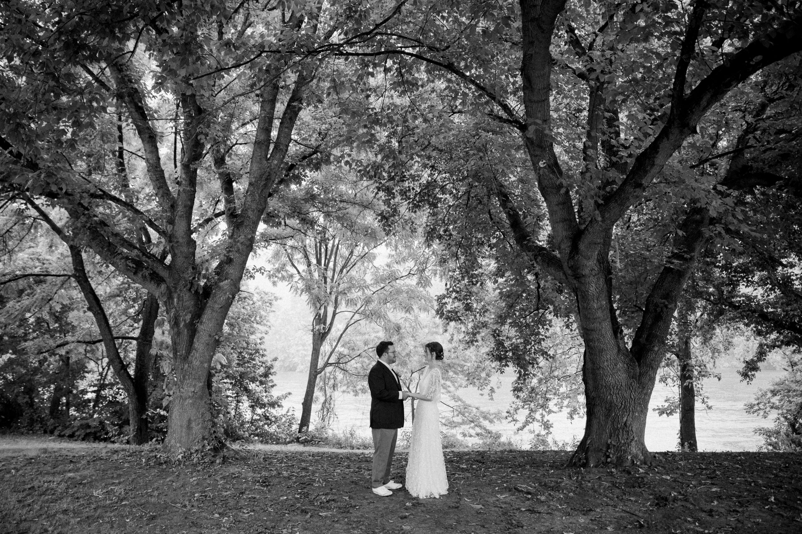 A black and white picture of a coupld holding hands and looking at each other surrounded by trees at Low Water Bridge Campground