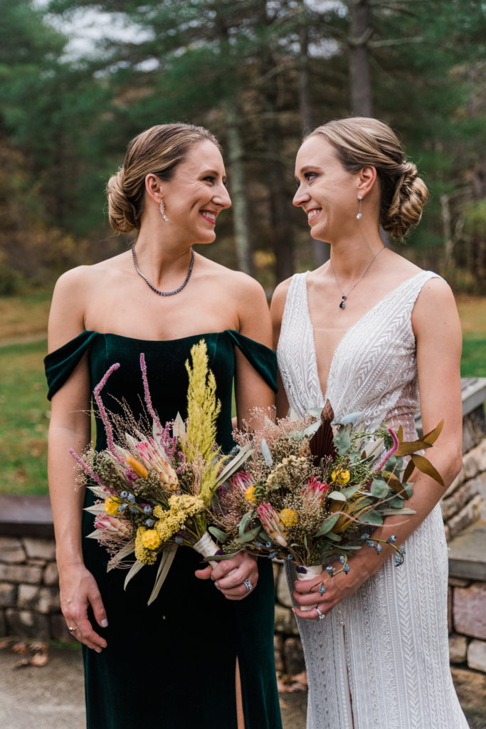 A bride poses with a bridesmaid outside