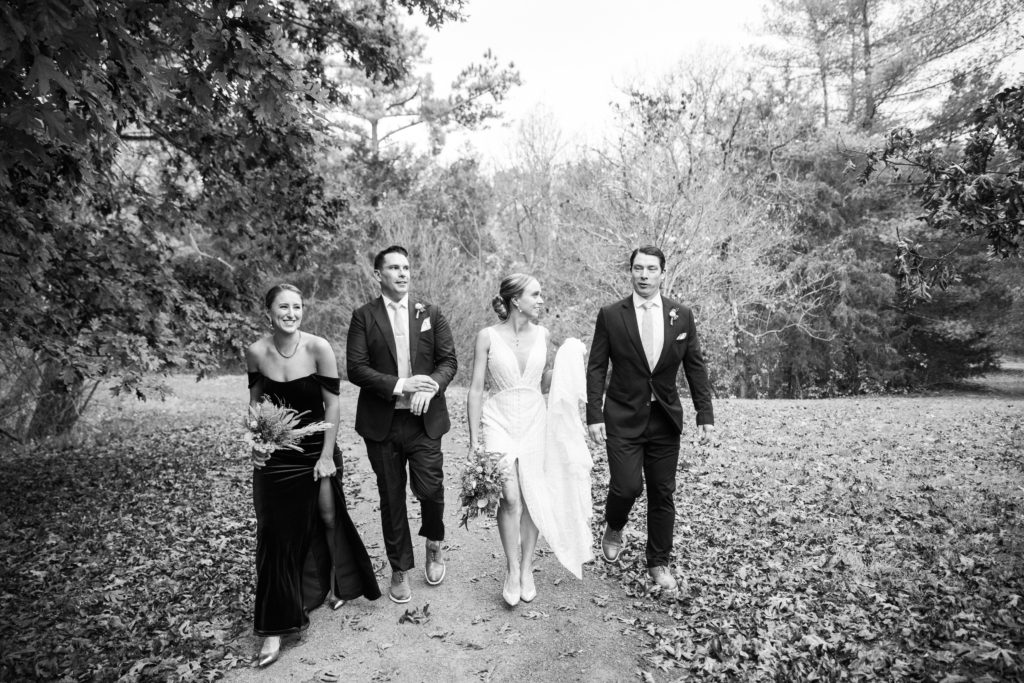 Four people walking through the woods wearing wedding attire