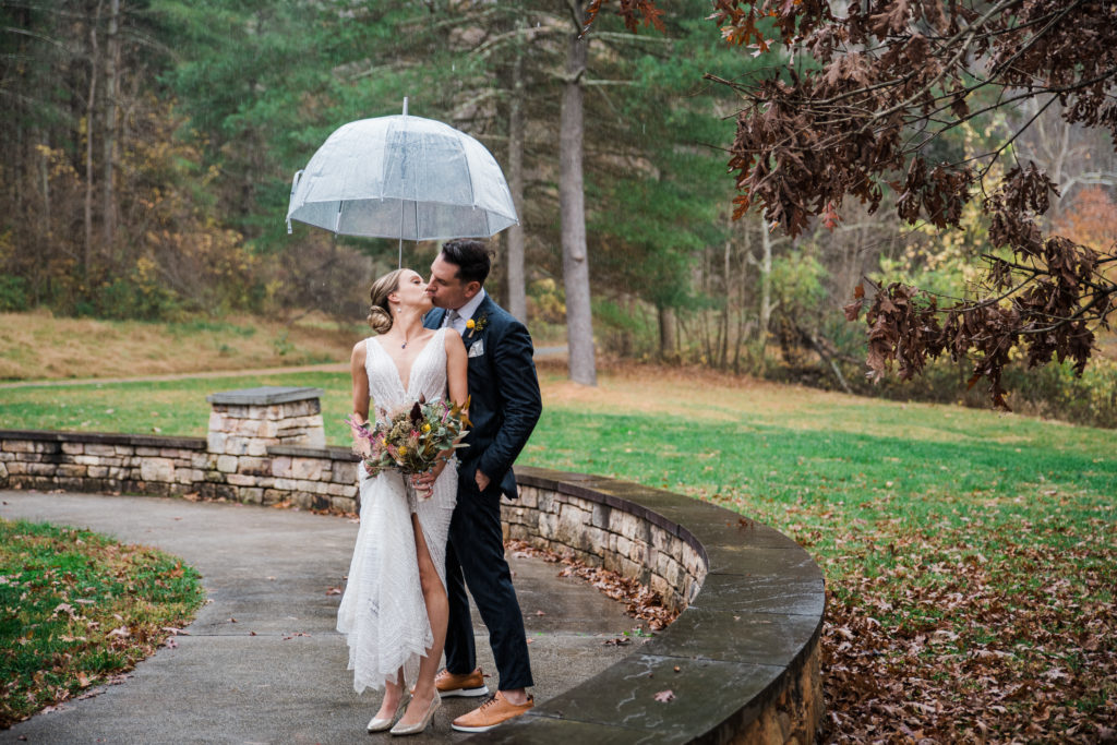 A bride and groom kiss under an umbrella