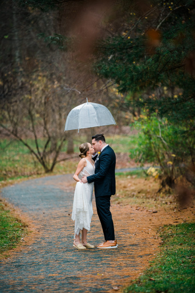 A bride and groom stand under an umbrella kissing