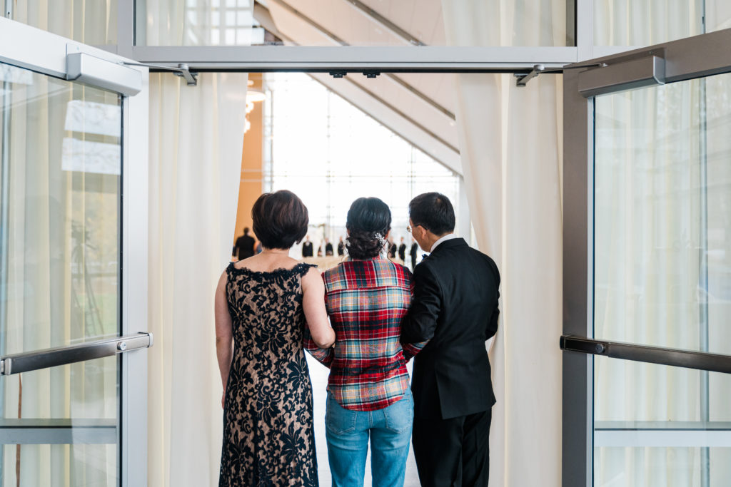 Three people stand with their backs to the camera waiting to enter a room