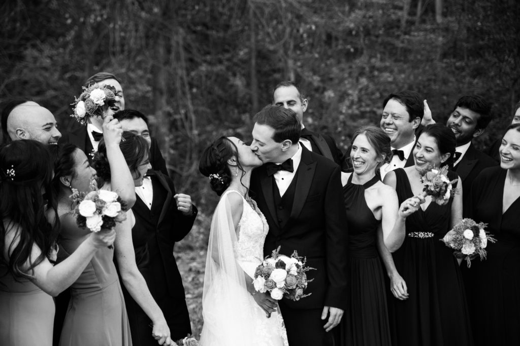 A bride and groom kiss in front of their wedding party