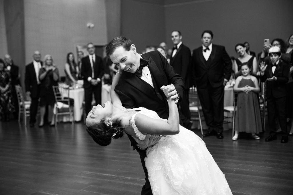 A black and white picture of a groom dipping a bride on the dance floor