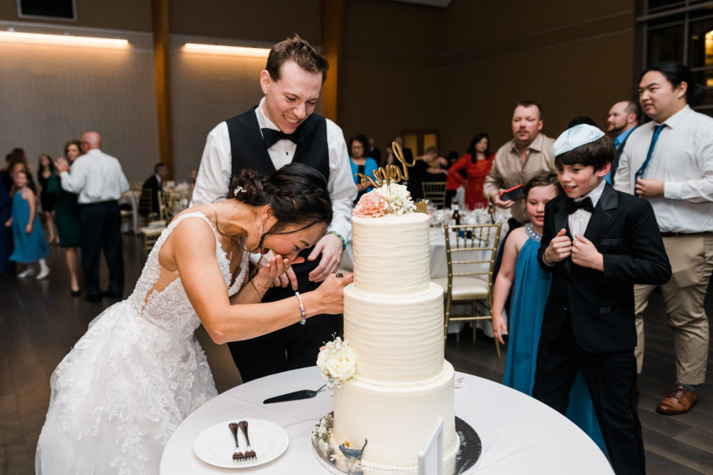 A bride and groom laughing while cutting a wedding cake