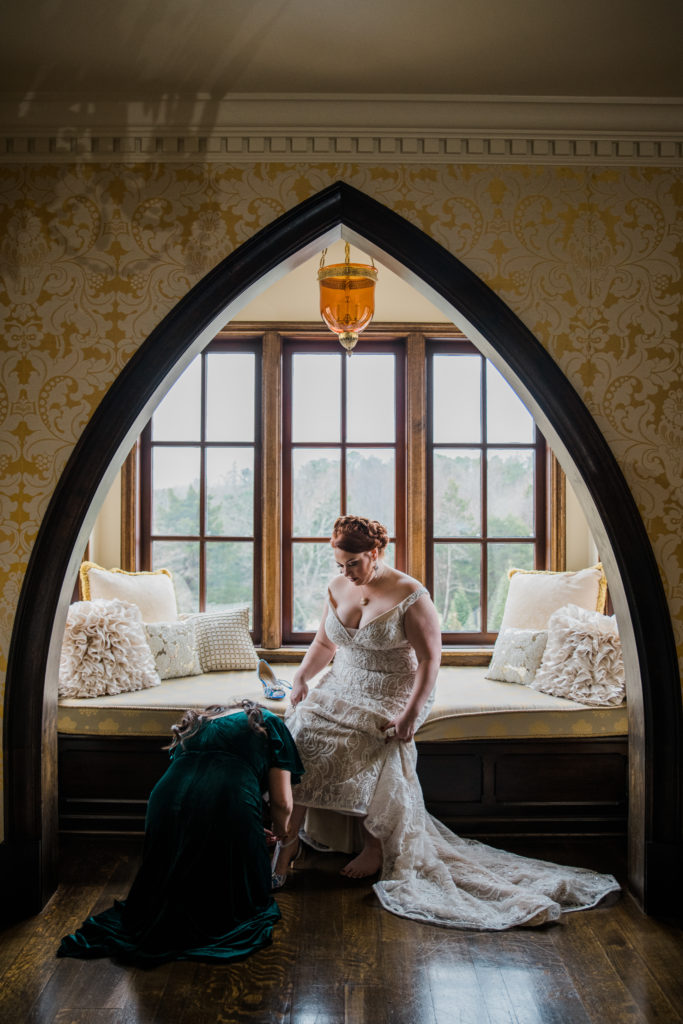 A woman in green helps a bride in white put her shoes on