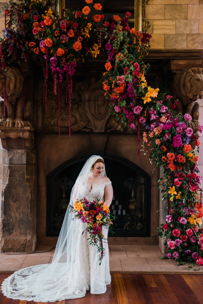 A bride posing in front of a large fireplace decorated with colorful flowers
