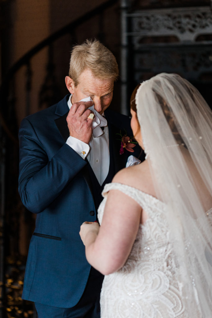 A man dabbing his eyes with a napkin while standing with a bride