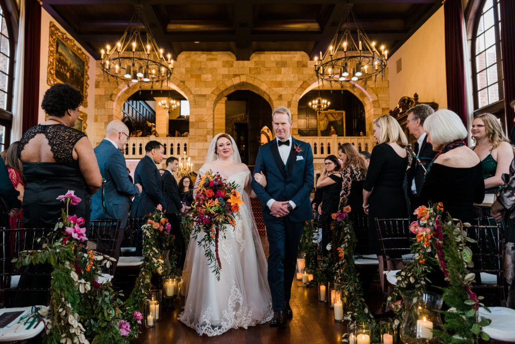 A bride walks down the aisle on the arm of a tall man