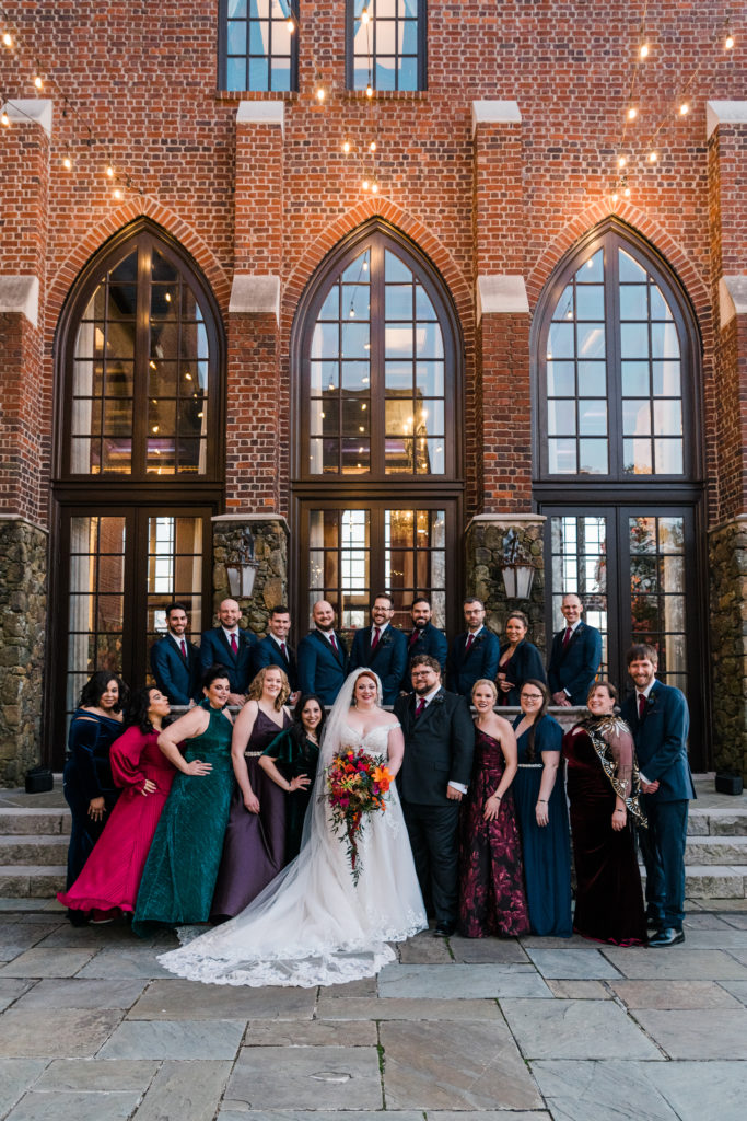 A wedding party poses outside a building with large windows