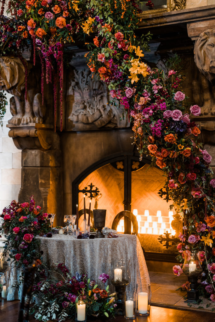 A table in front of a large fireplace with colorful flowers on the table and fireplace