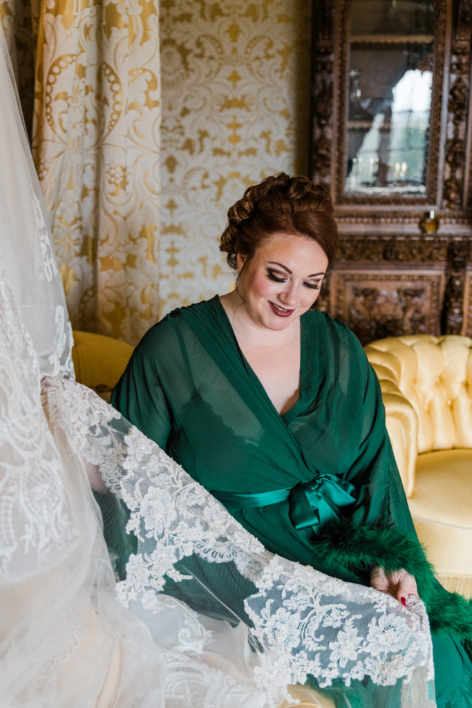 A woman in a green robe touching the lace on a wedding dress