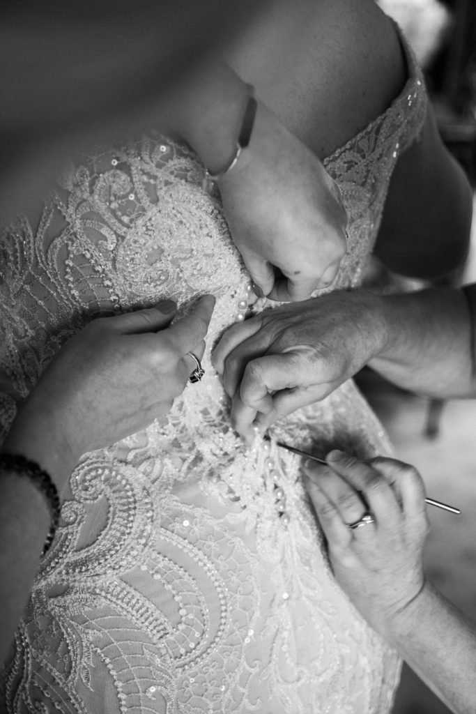 Black and white close up picture of hands helping to button up a wedding dress