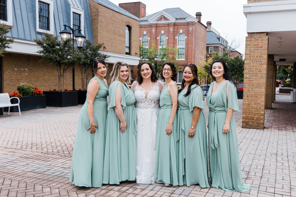 A bride posing with bridesmaids in green dresses
