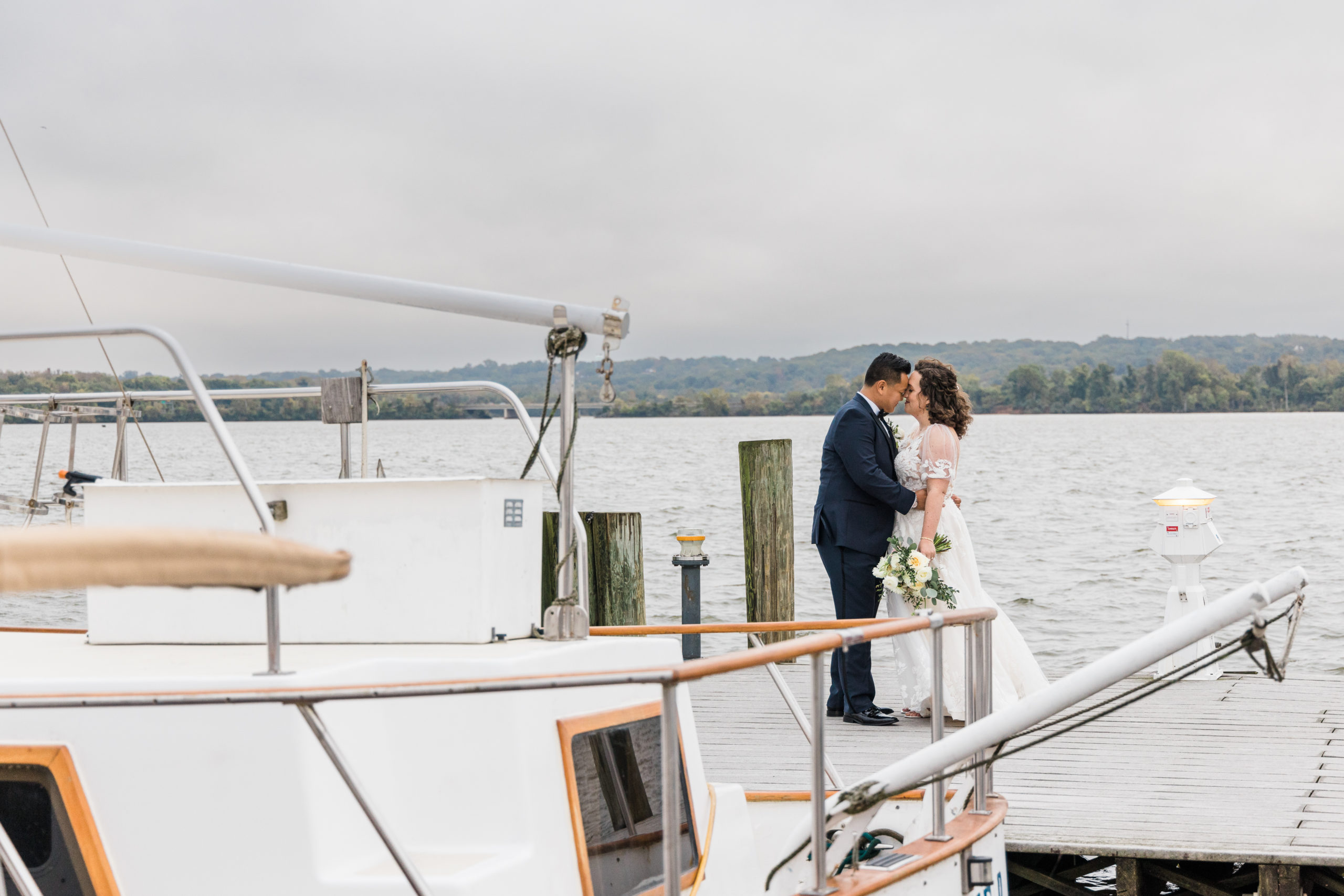 A bride and groom kiss on the dock by a boat
