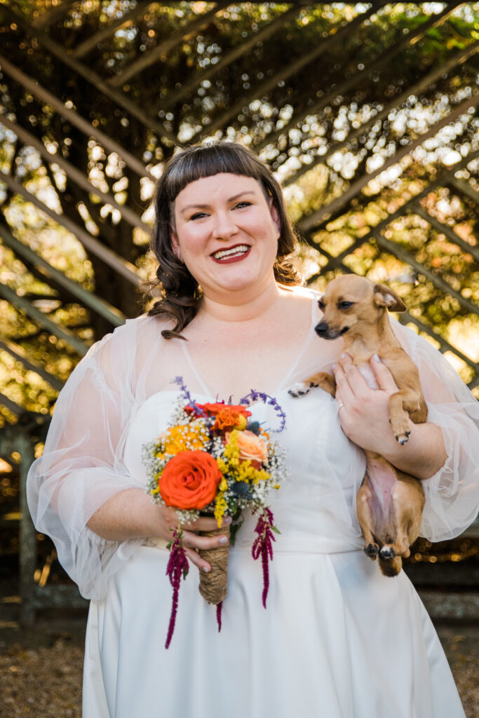 A bride smiling and holding a small dog