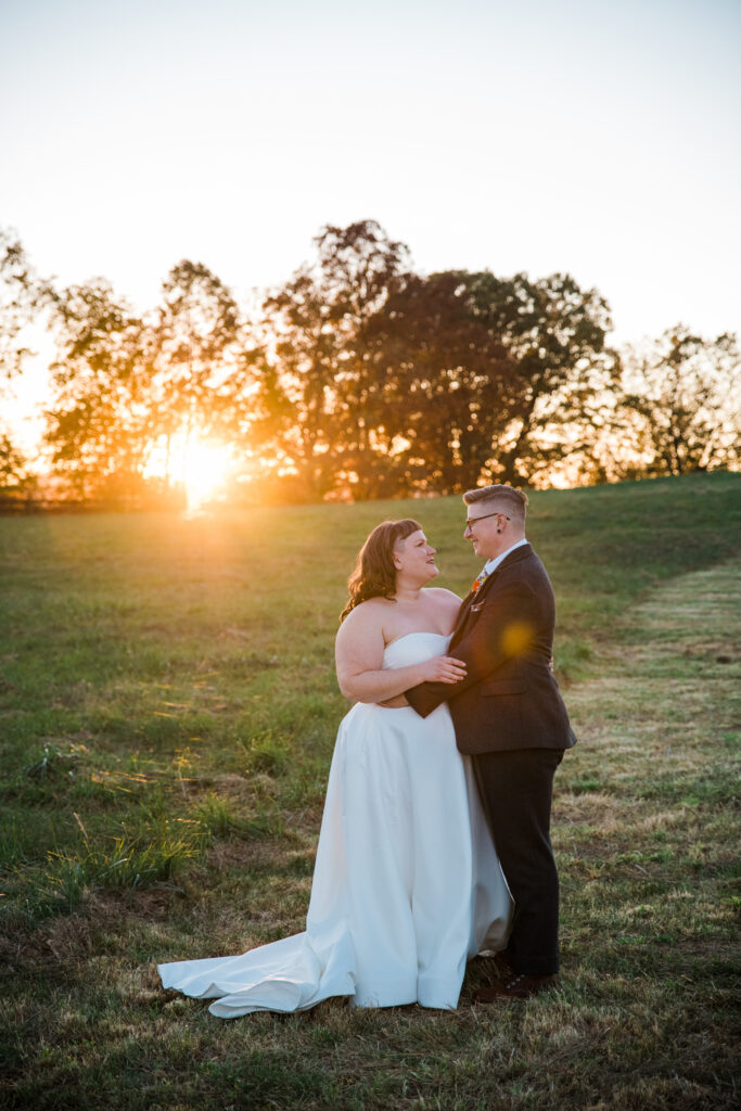 A couple hugging in a field as the sun sets behind them