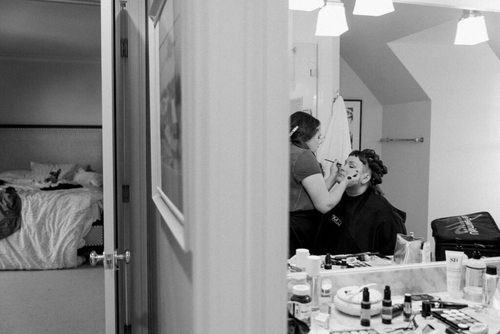 A woman sits in a chair having her make up applied