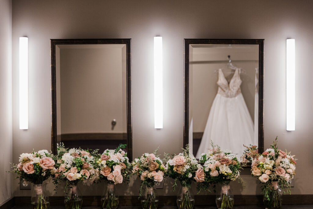 A reflection in a mirror of a wedding dress hanging up with bouquets of flowers underneath it