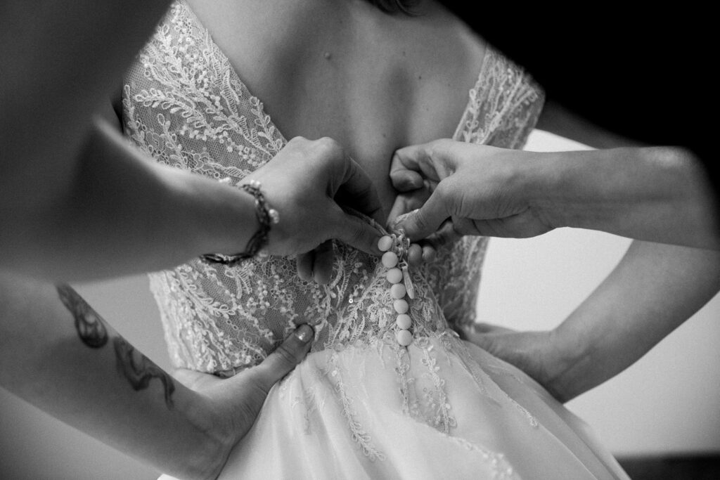 A black and white photo of the back of a bride's dress being buttoned up
