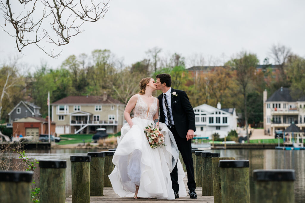 A man in a suit and a woman in a wedding dress kissing on a dock 