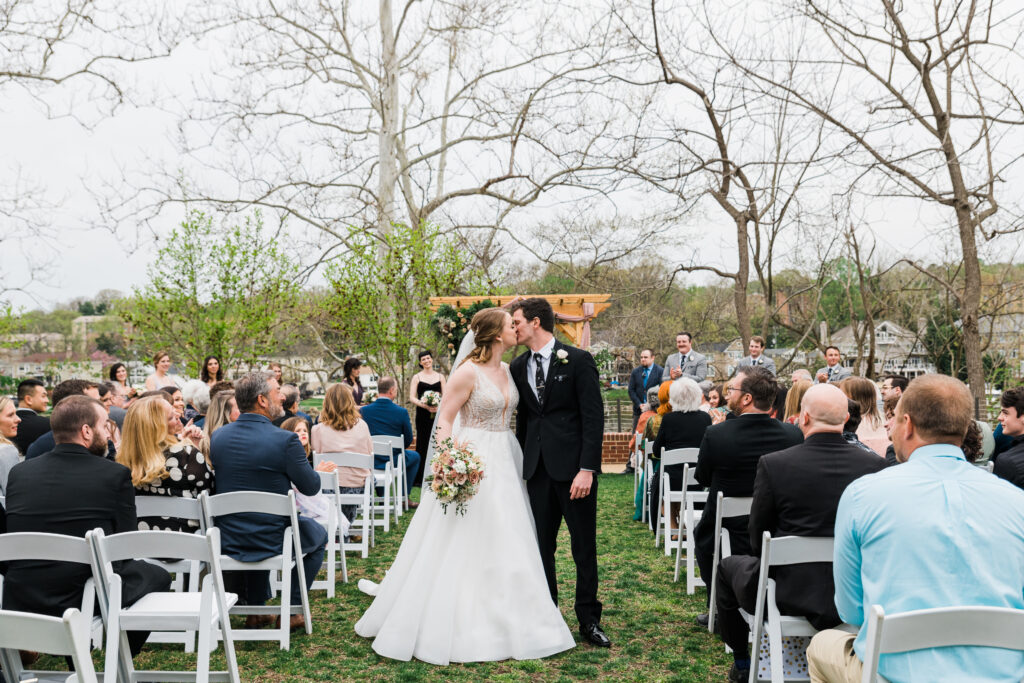 A bride and groom kissing an aisle surrounded by people sitting in chairs