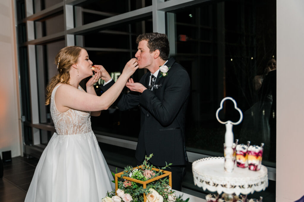 A man in a suit and a woman in a wedding dress feeding each other cake