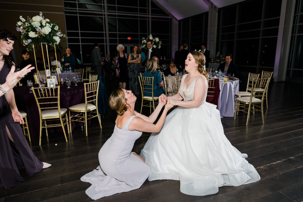 A woman in a dress kneeling in front of a woman wearing a wedding dress