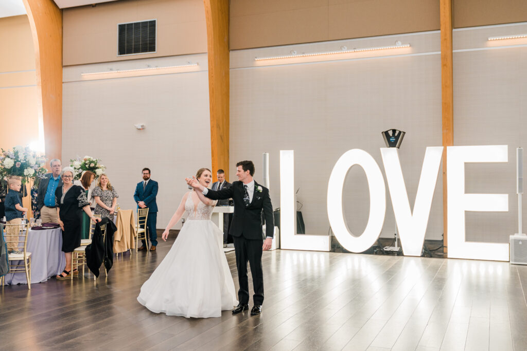 A man in a suit and a woman in a wedding dress standing in front of a large white sign that says Love